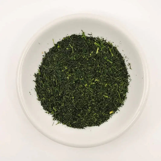 Green tea leaves in a white bowl on a white background