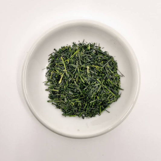 Green tea leaves in a white bowl on a light gray background