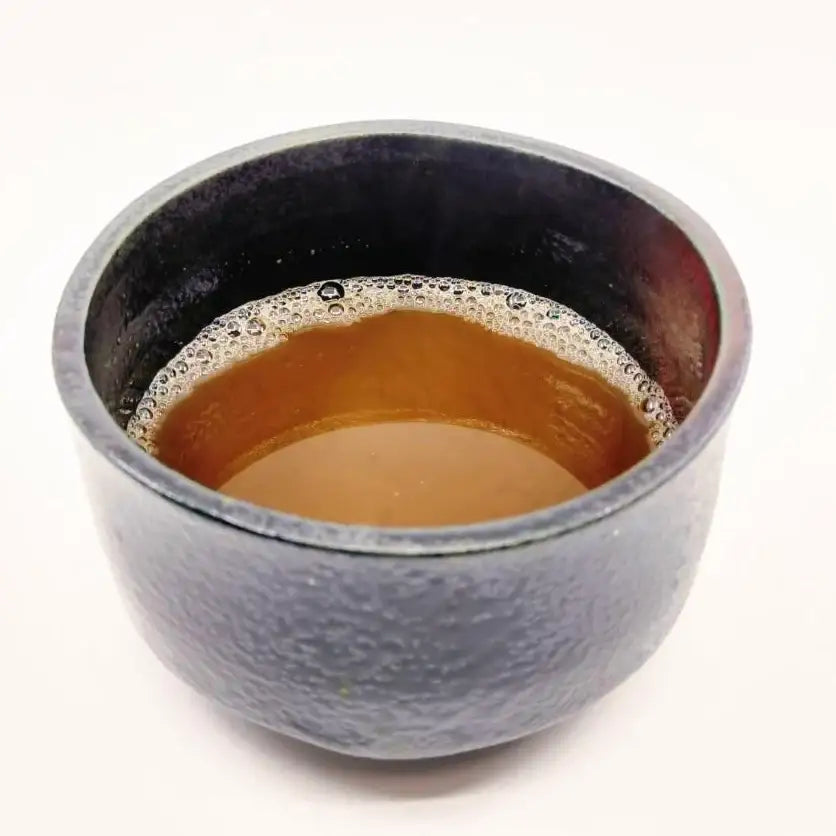 Japanese tea in a textured ceramic cup with rich amber brew and delicate foam