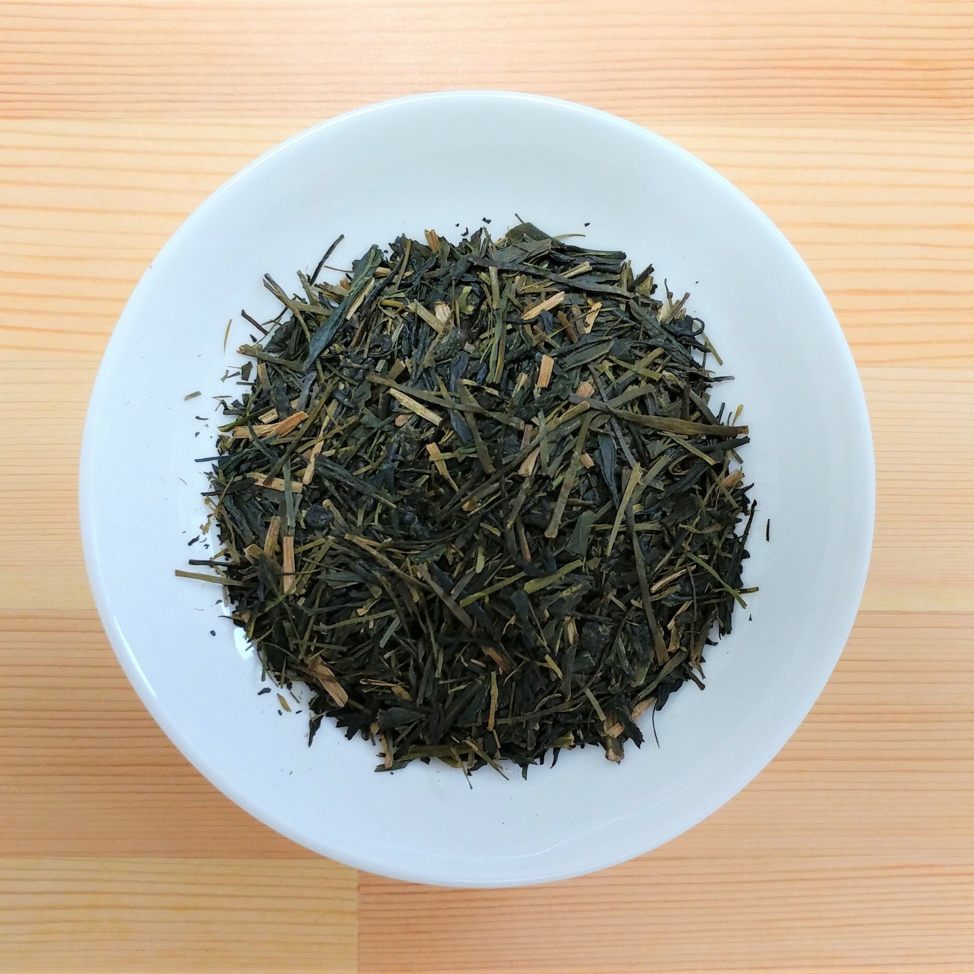 Dry green tea leaves on a white plate with a wooden background