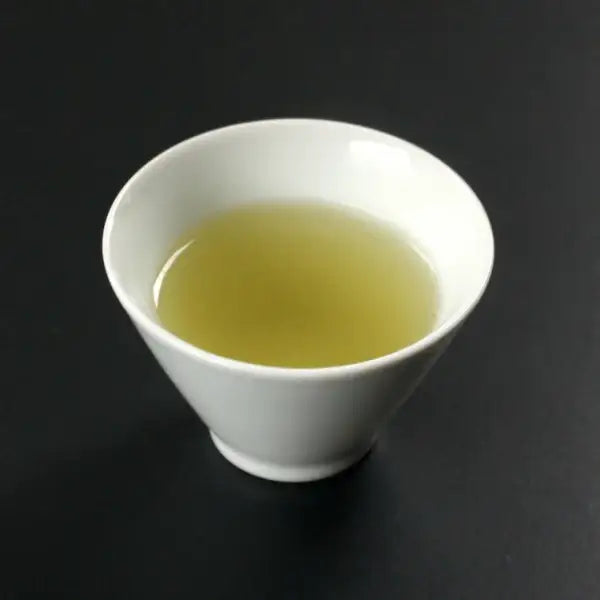White ceramic tea cup filled with light green Japanese green tea on dark background
