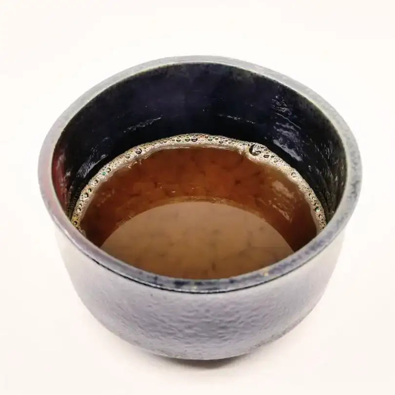 Handcrafted Japanese teacup with rich tea, showcasing artisanal ceramic texture and deep glaze
