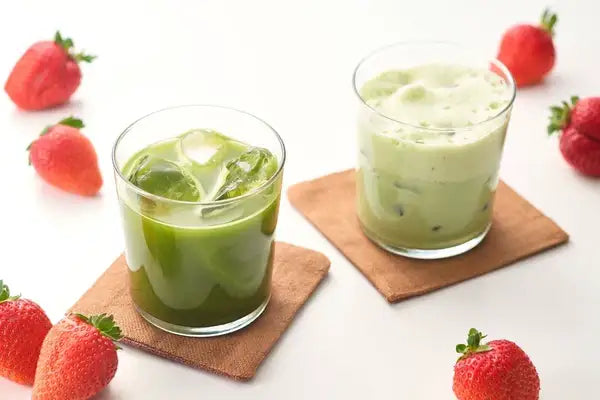 Iced matcha green tea with ice cubes and frothy matcha latte, surrounded by fresh strawberries on a white background.