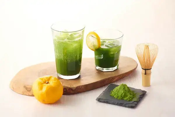 Iced green tea with lemon, matcha powder, and bamboo whisk on wooden tray