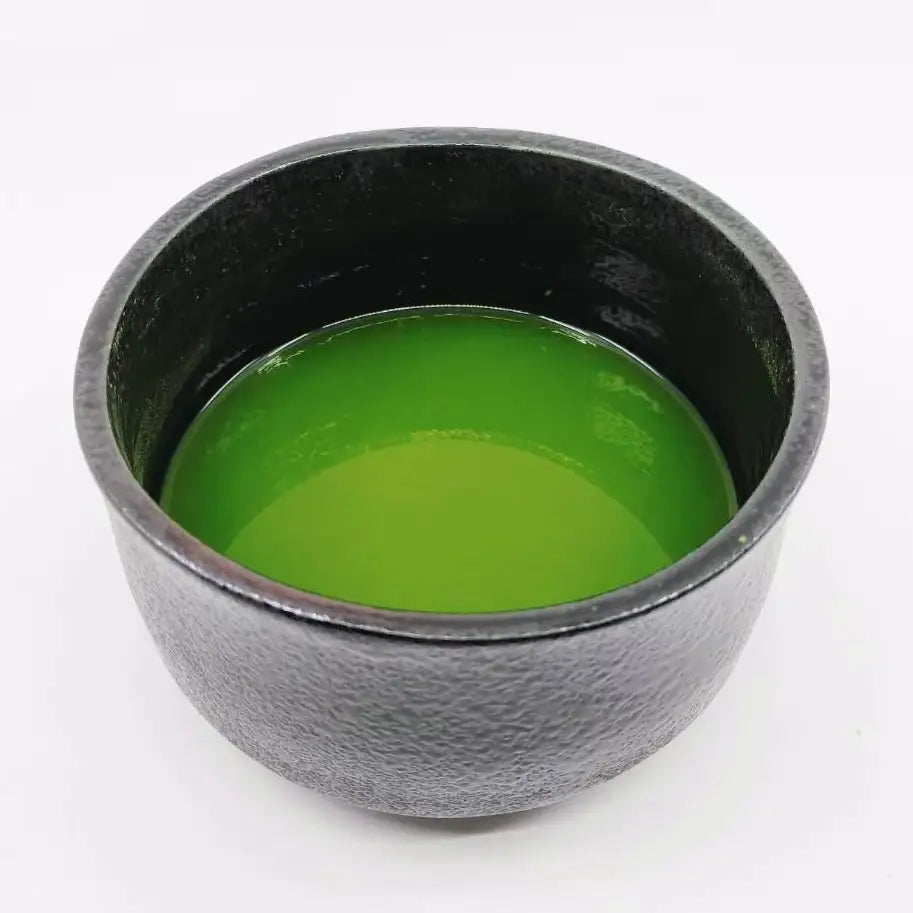 Vibrant green matcha tea in a textured black ceramic bowl, showcasing authentic Japanese tea culture.