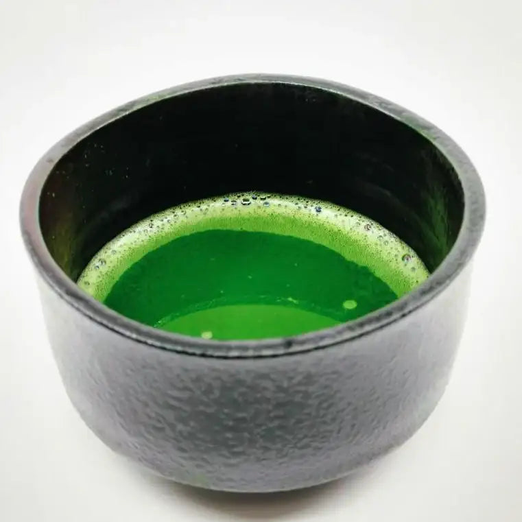 Black ceramic chawan bowl filled with vibrant green Japanese matcha tea on white background
