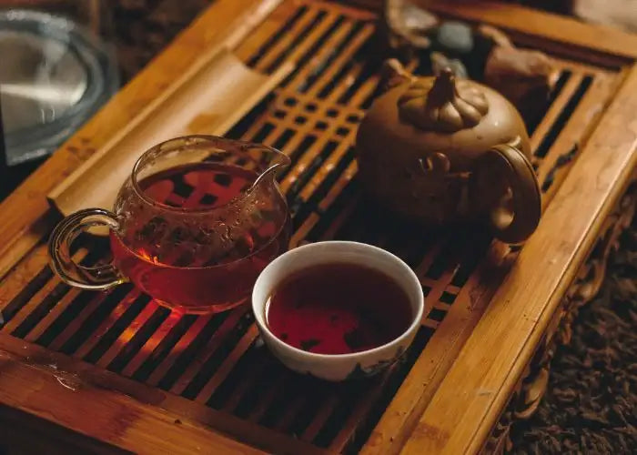Japanese tea set with ceramic teapot, glass pitcher, and cup on bamboo tray, showcasing rich amber tea