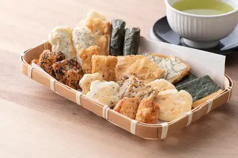Assorted Japanese rice crackers in basket with green tea on wooden table