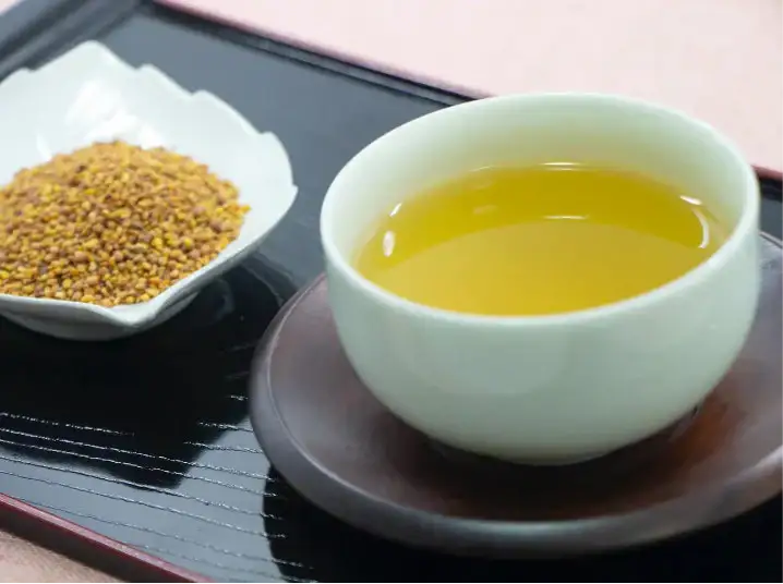 Cup of golden Japanese tea with roasted tea leaves on a black tray