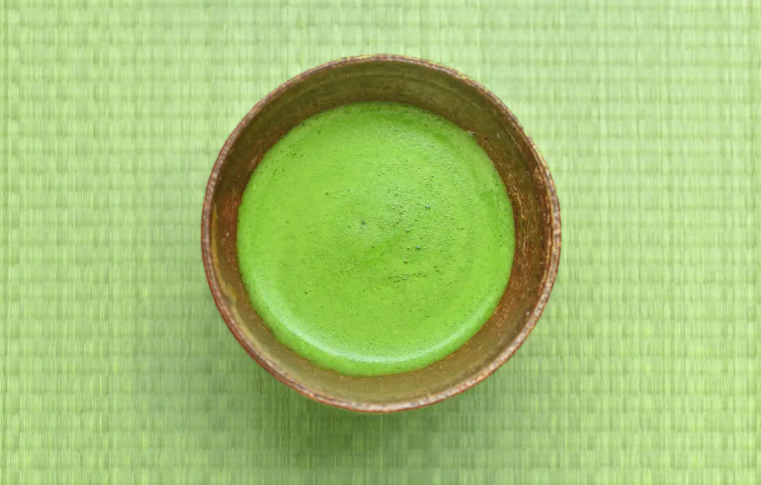 Ceramic bowl of frothy matcha green tea on a woven green mat