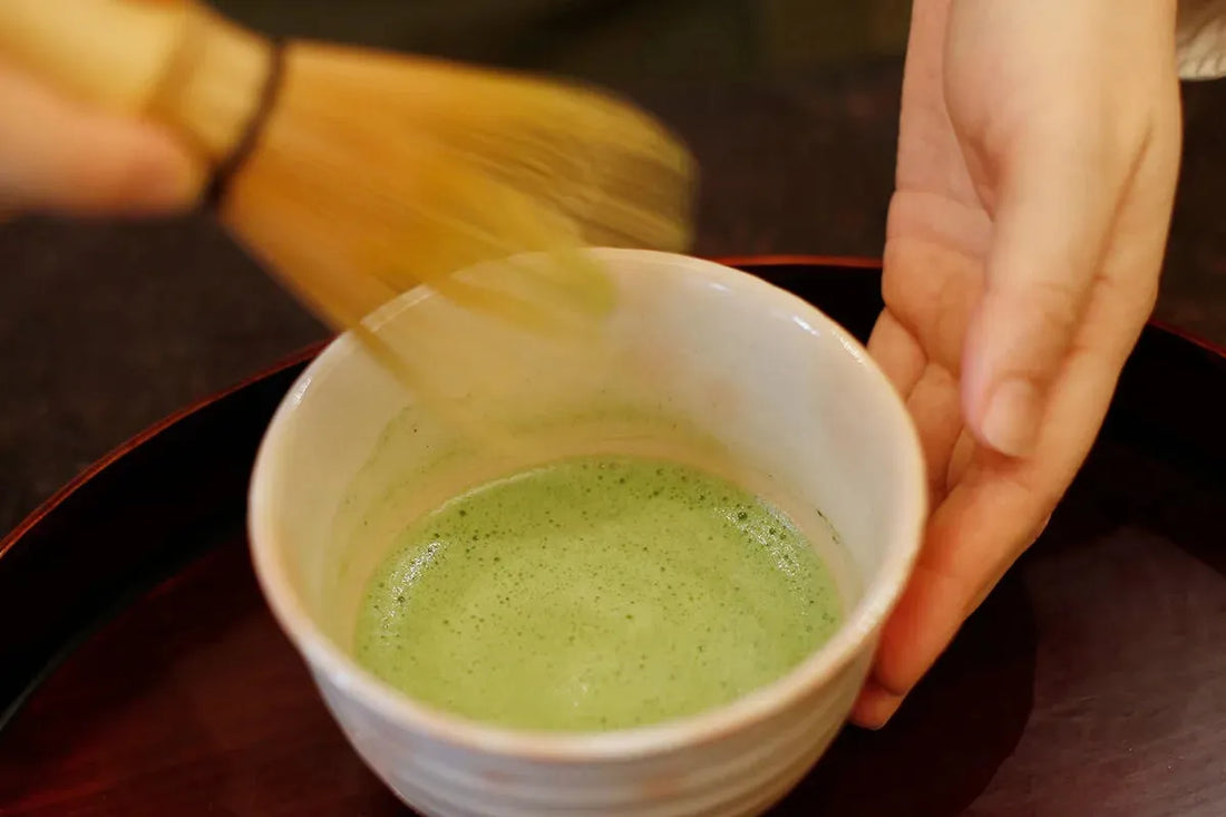 Whisking vibrant green matcha tea in a ceramic bowl with bamboo chasen, showcasing traditional Japanese tea preparation.