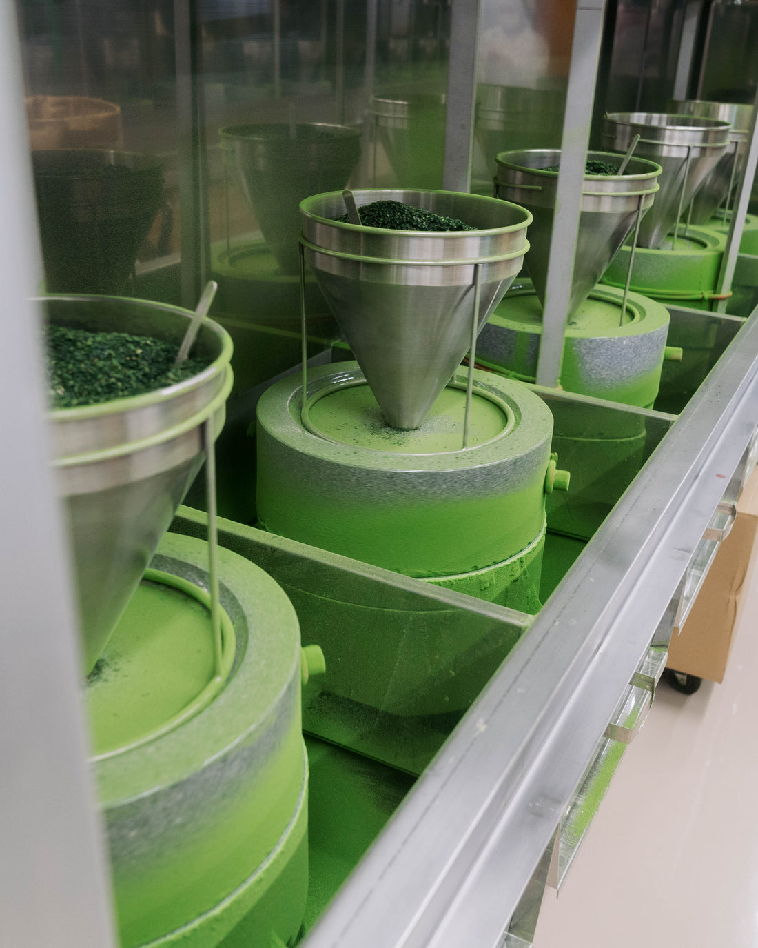 Traditional stone mills grinding green matcha tea leaves in a modern facility