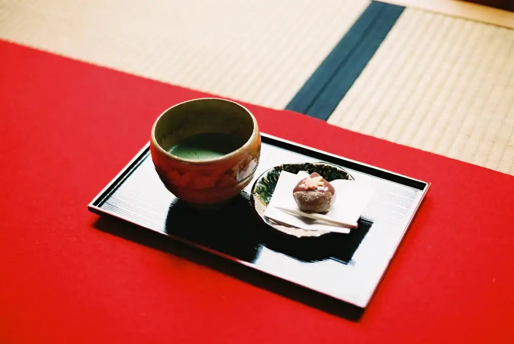 Japanese matcha tea and wagashi dessert on a tray, set on tatami mat with red cloth