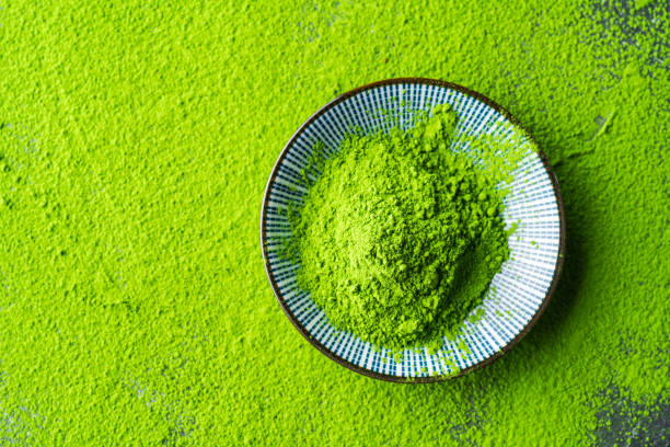 Vibrant green matcha powder in a ceramic bowl, surrounded by loose tea dust for authentic Japanese tea experience
