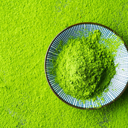 Vibrant green matcha powder piled in a ceramic bowl on a textured matcha background