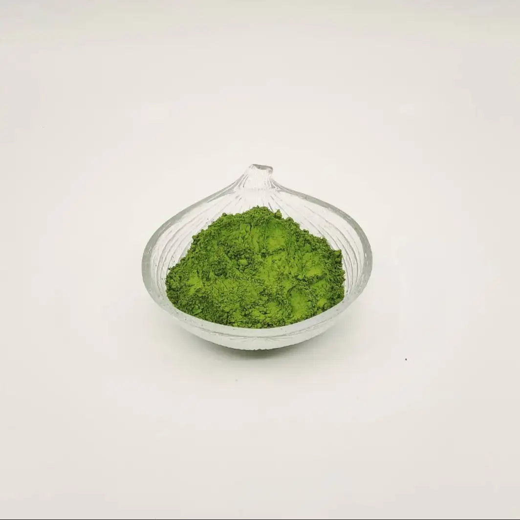 Green powder in a glass container on a white background