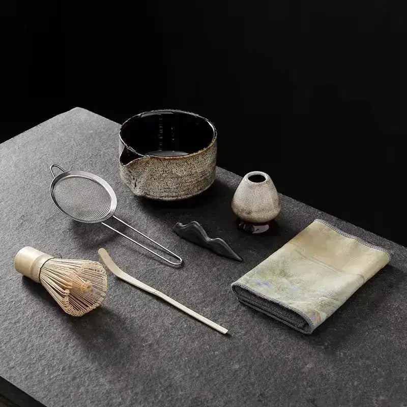 Japanese matcha tea set with whisk, sieve, ceramic bowl, and teaware on dark stone surface
