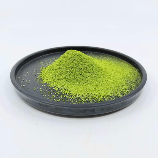 Pile of vibrant green Japanese matcha powder on a black plate against a white background