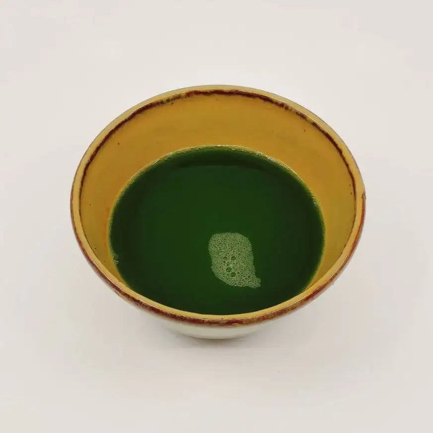 Ceramic cup with gold rim containing green liquid on a white background