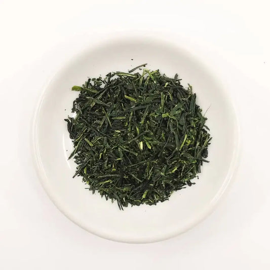Green tea leaves in a white bowl on a white background