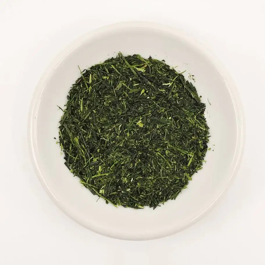 Green tea leaves in a white bowl on a white background