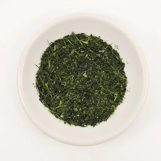 Green tea leaves in a white bowl on a white background
