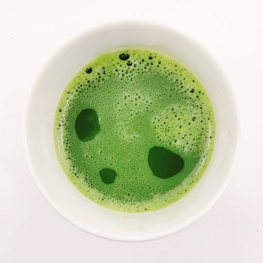 Green frothy beverage in a white bowl on a white background