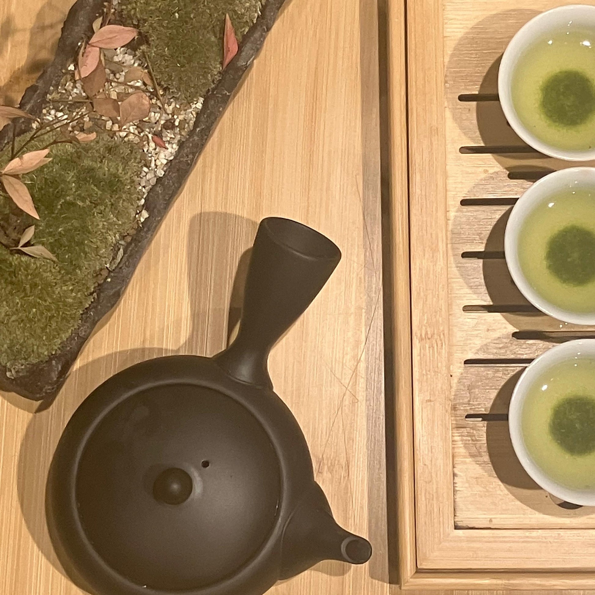 Tea set with a black teapot and three cups of green tea on a wooden surface.
