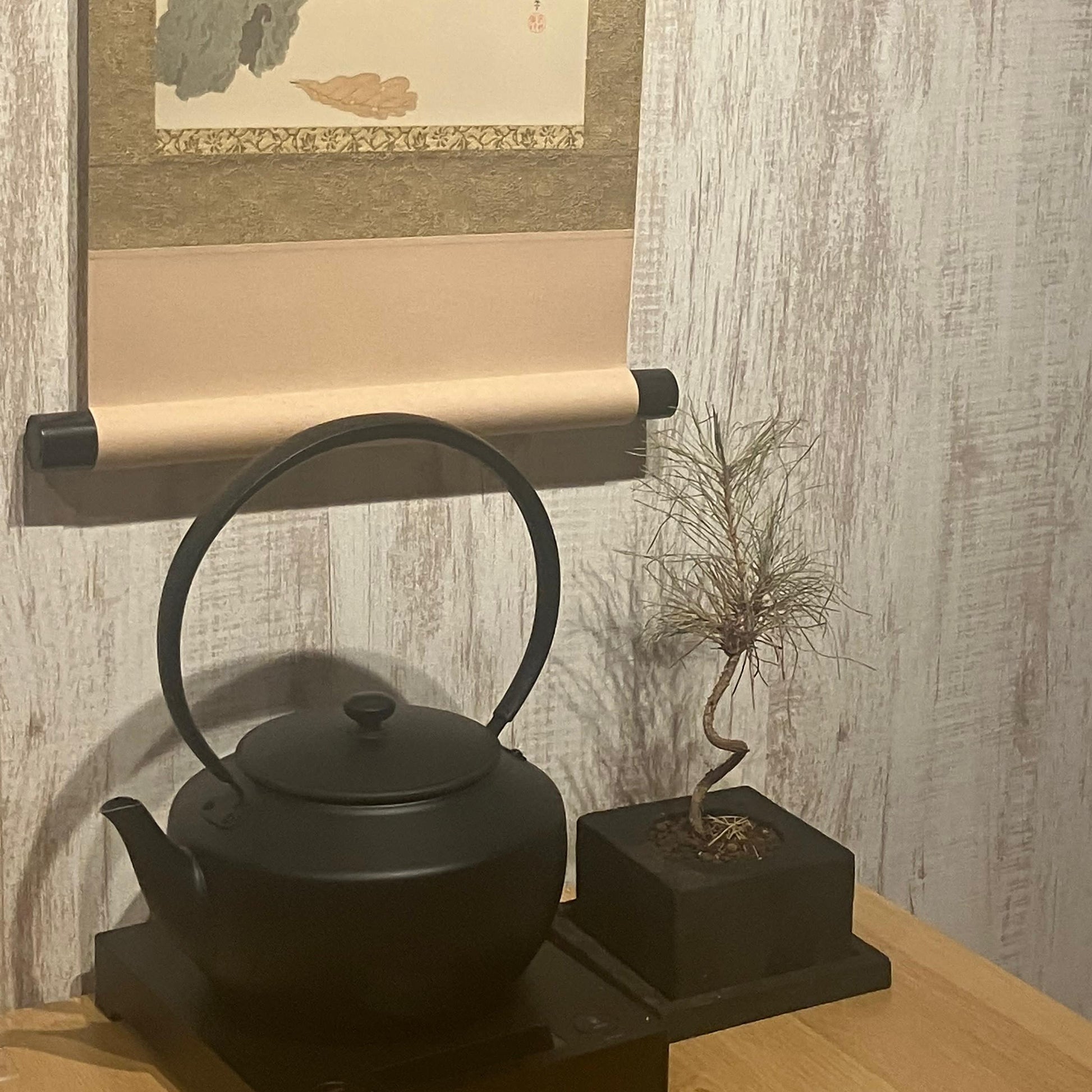 Black teapot on a wooden surface with a framed artwork of a cat in the background.