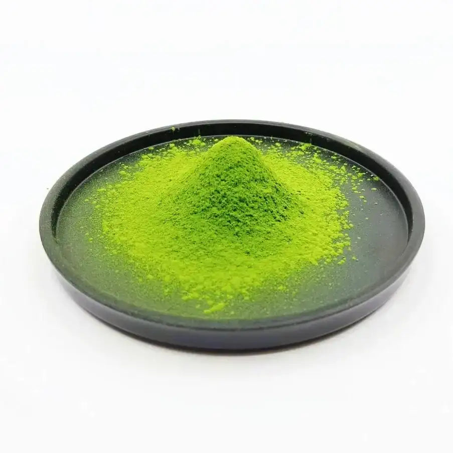 Vibrant green matcha powder piled on a dark ceramic dish, showcasing premium Japanese tea quality.
