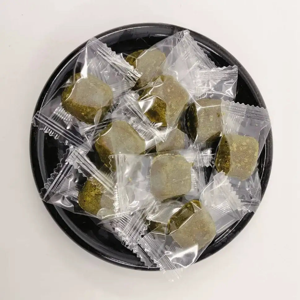 Individually wrapped Japanese matcha tea candies on a black plate, perfect for tea lovers
