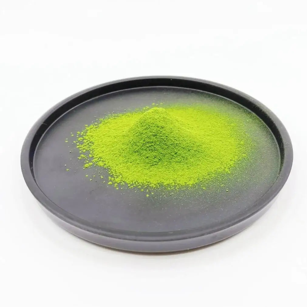 Vibrant green matcha powder piled on a dark ceramic dish, showcasing premium Japanese tea quality.