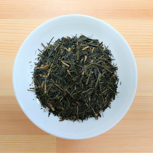 Dry green tea leaves on a white plate with a wooden background