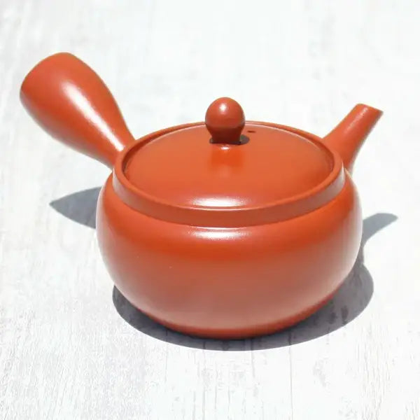 Handcrafted terracotta teapot for Japanese tea ceremonies, featuring smooth curves and a glossy finish.