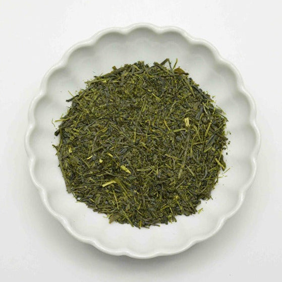Green tea leaves in a white ceramic bowl on a light gray background