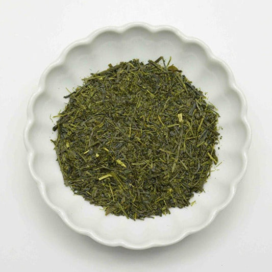 Green tea leaves in a white ceramic bowl on a light gray background
