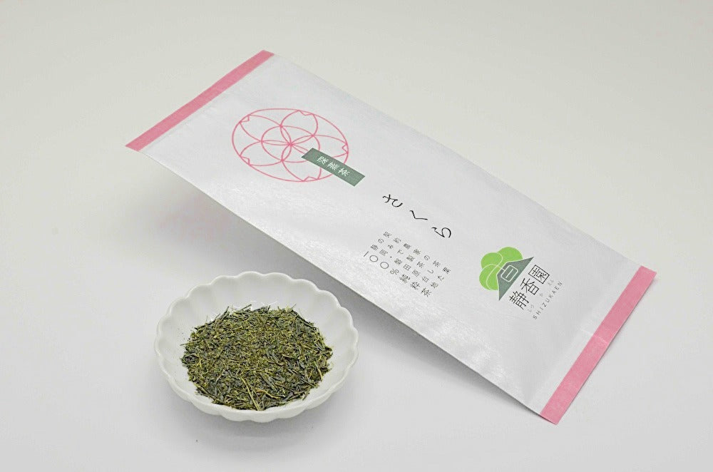 Tea leaves in a small white dish with a pink and white packaging on a light gray background