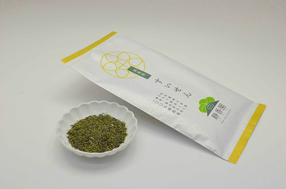 Green tea leaves in a small white dish with a packaging box on a light gray background