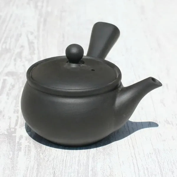 Black ceramic Japanese teapot with lid, spout, and handle on light wood surface