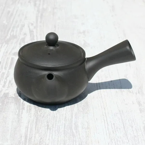 Black ceramic Japanese teapot with lid and spout on light wood surface