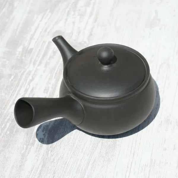 Black ceramic Japanese teapot with side spout on light wood surface