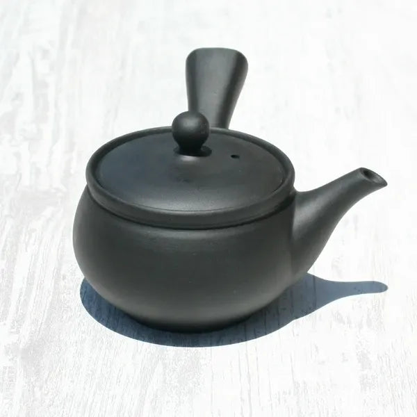 Black ceramic Japanese teapot with lid and handle on white wood surface
