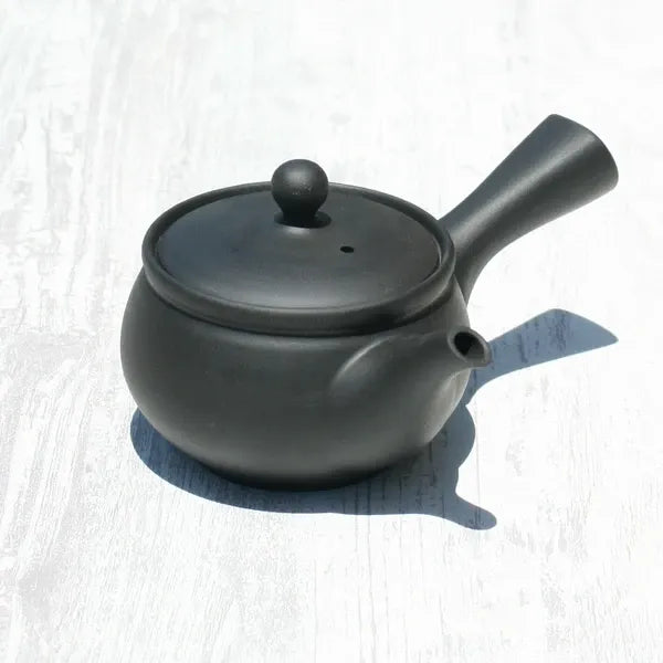 Black ceramic Japanese teapot with lid, perfect for brewing premium tea on white wood surface