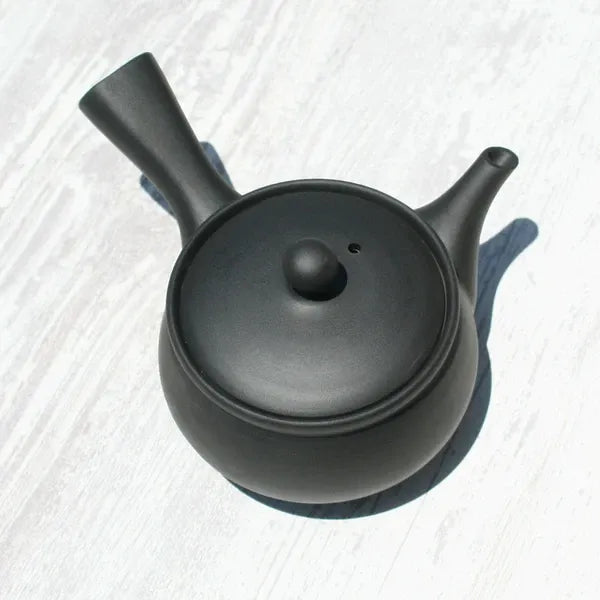 Black ceramic Japanese teapot with lid on light wood surface, ideal for premium tea brewing