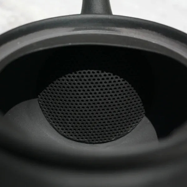 Close-up of black ceramic teapot interior with fine mesh strainer for loose leaf tea brewing
