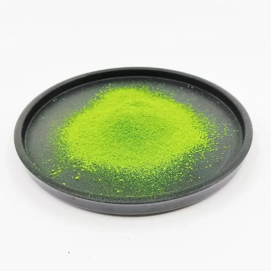 Vibrant green matcha tea powder on a round black plate, isolated on white background
