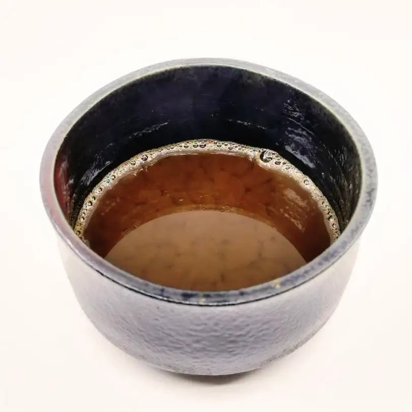 Handcrafted Japanese teacup with dark glaze, filled with rich brown tea, showcasing artisanal design.