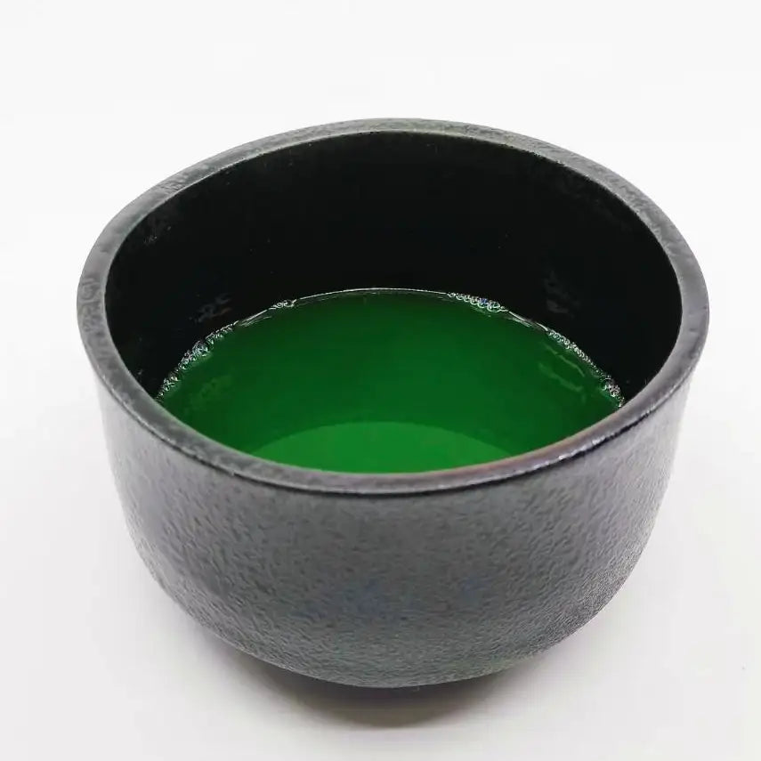 Black textured ceramic tea bowl filled with vibrant green matcha, showcasing Japanese tea culture.