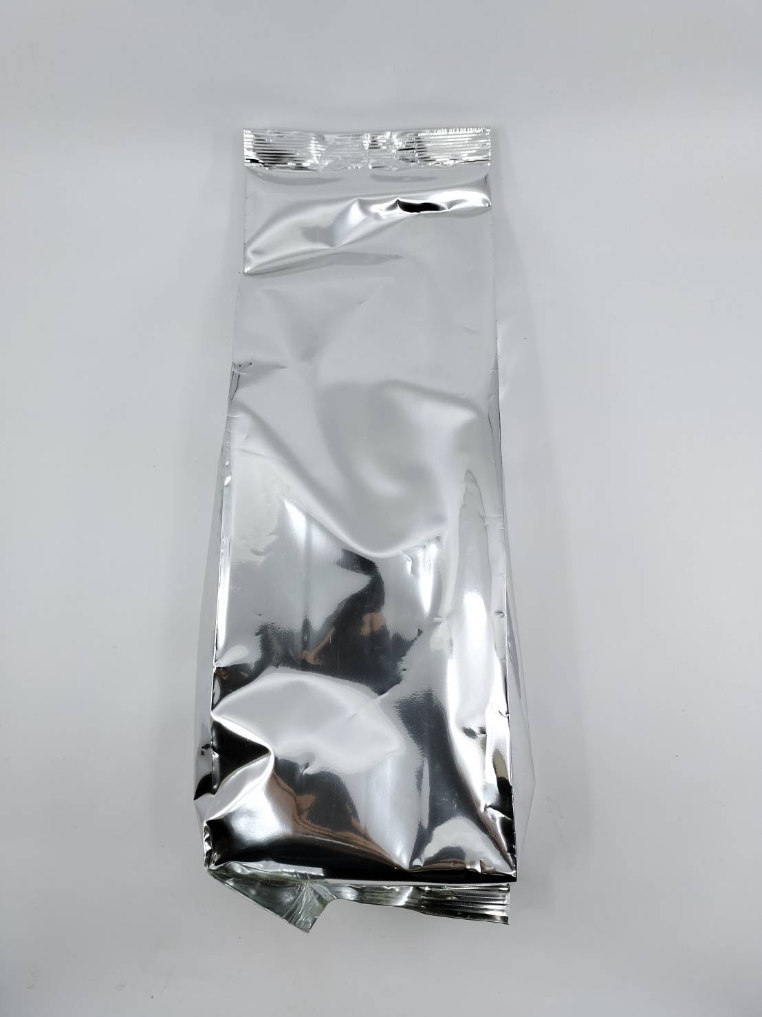 Shiny silver foil tea bag packaging for premium Japanese tea, sealed and crinkled on white background