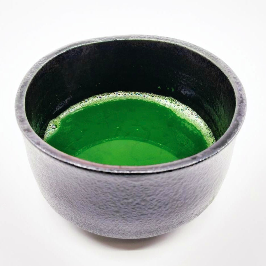 Vibrant green matcha tea in a textured gray ceramic bowl, showcasing authentic Japanese tea culture.